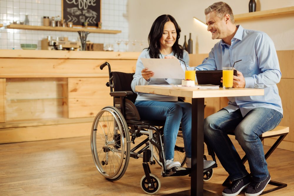 A woman in a wheelchair sitting with a man at a desk happily discussing her disability income protection policy